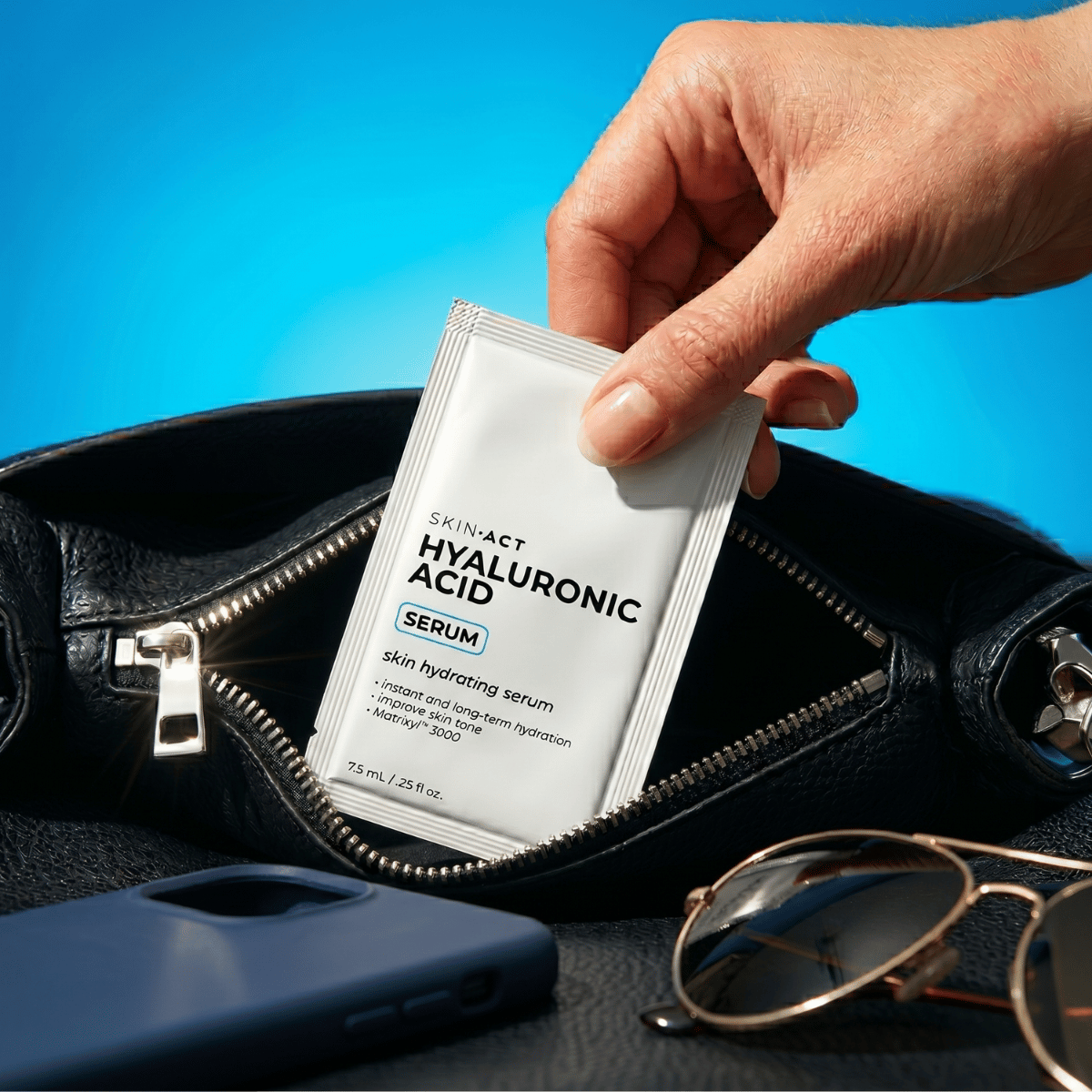 Hand holding a Skin-Act Hyaluronic Acid Serum packet with a blue background