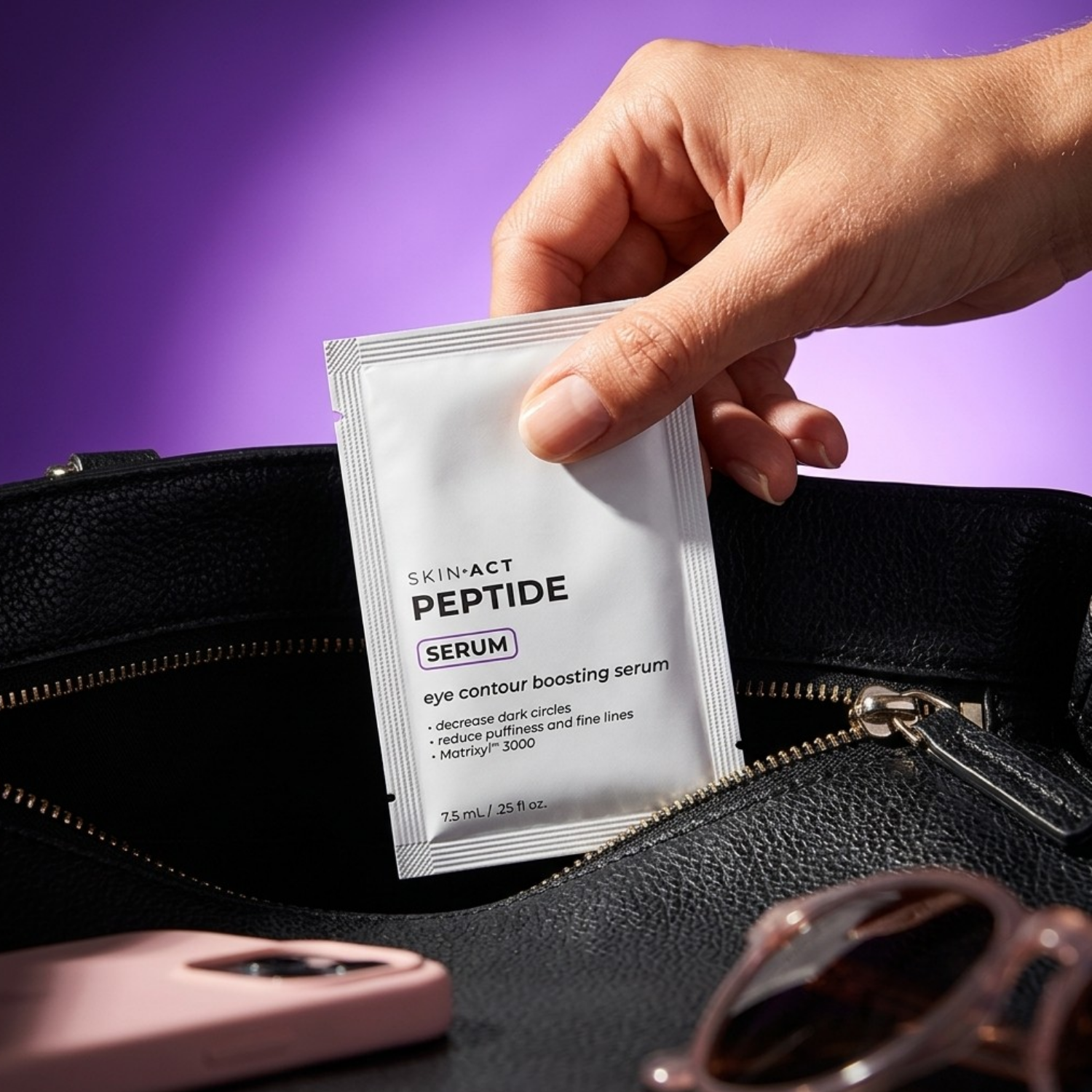 Hand holding a Skin-Act Peptide Serum packet over a black handbag with sunglasses on a purple background